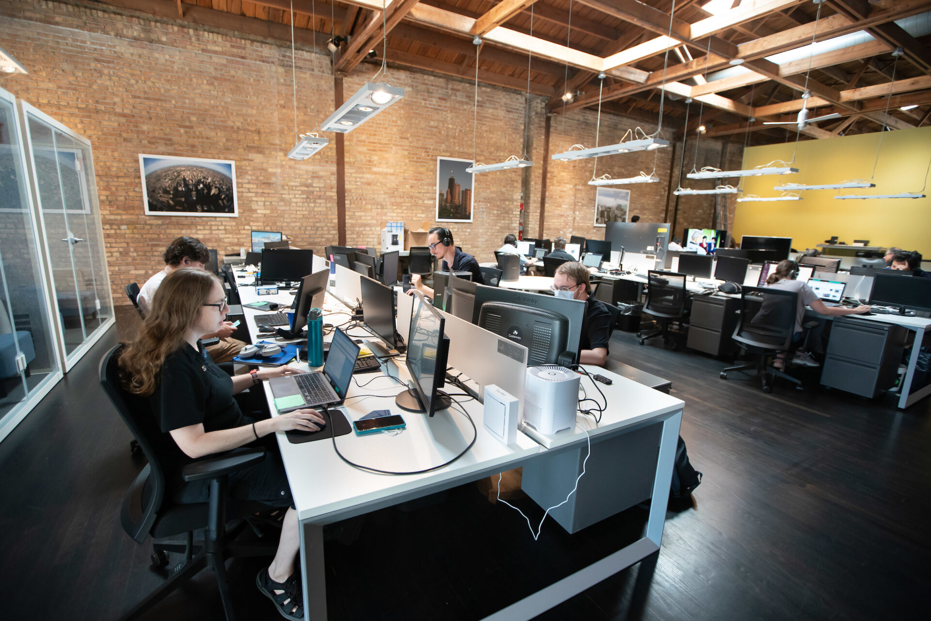 Aspiritech employees work at computers on both sides of a long desk in an open office.