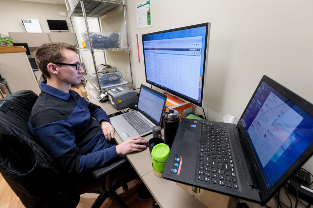 Young white professional at a desk with multiple laptops and computer screens surrounding him