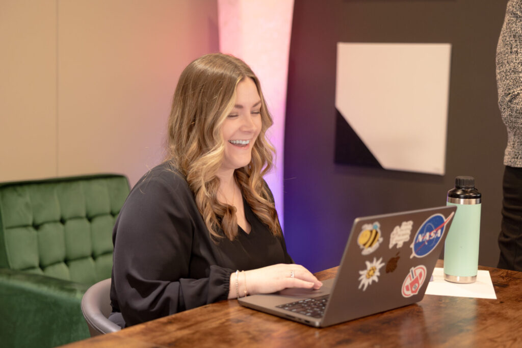 A female Aspiritech executive smiles at a laptop in a modern office space.