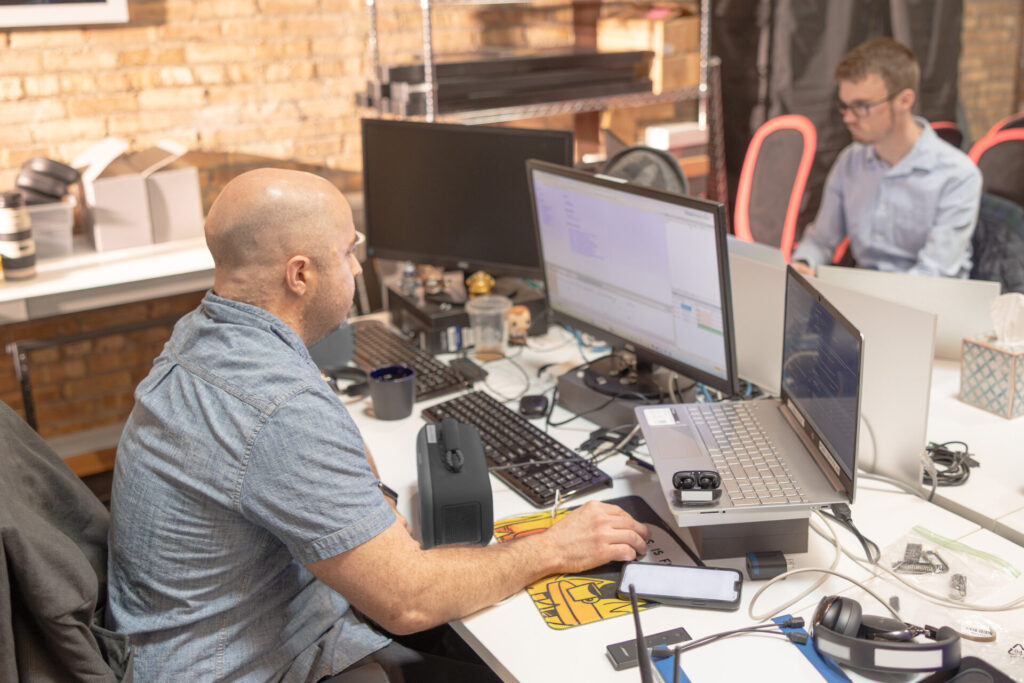 Two male Aspiritech employees work at computers on either side of a long desk.
